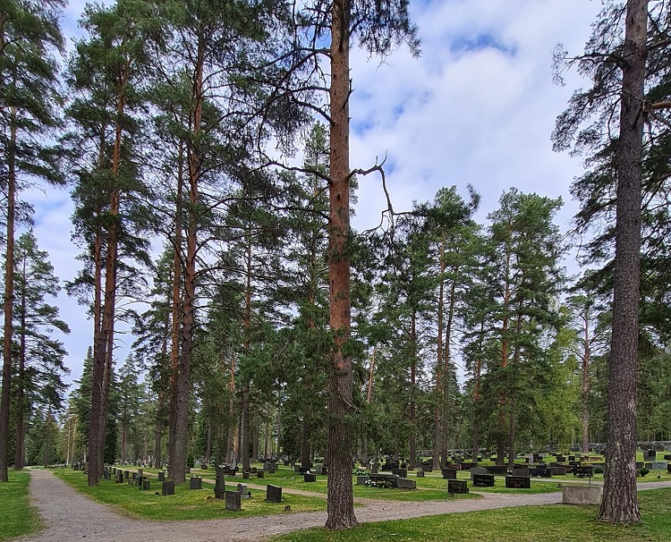 Hautausmaa, jossa hautakivien väleissä nurmikkoa ja mäntyjä. Hiekkakäytävät.