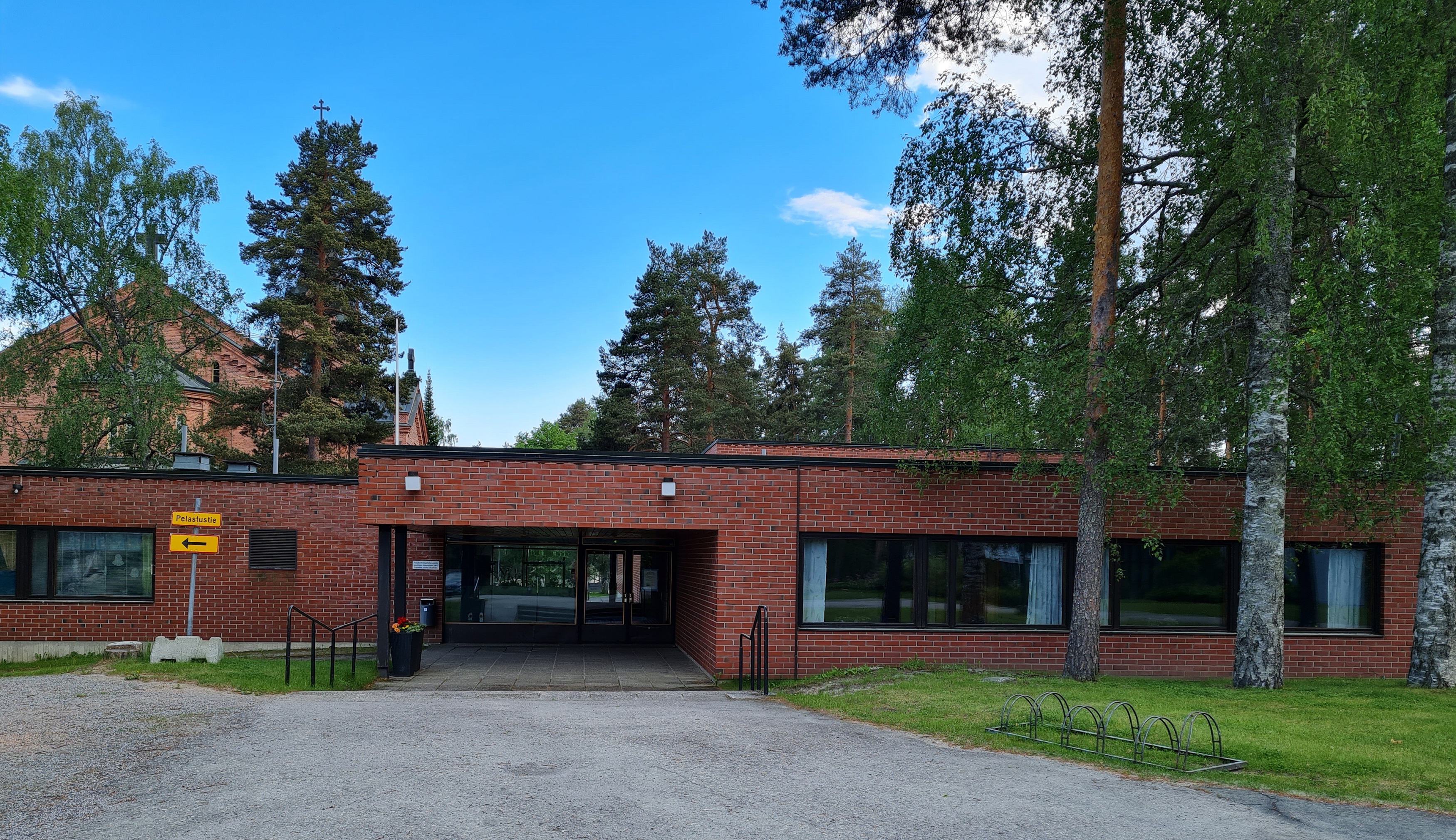 Tasakattoinen punatiilirakennus. Pääsisäänkäynnissä suuri ikkuna. 